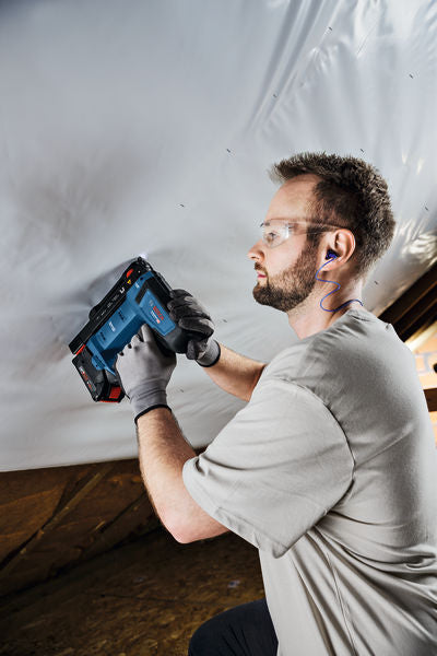 Eine Person mit Sicherheitsausrüstung befestigt mit einem Akkuwerkzeug Material an einer Decke.