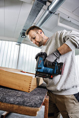 Eine Person mit Sicherheitsausrüstung befestigt Holzverbindungen mit einem Akku-Nagler.