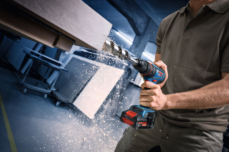 Person bohrt mit Akku-Bohrschrauber in Holz, Holzspäne fliegen