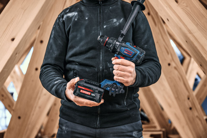Eine Person mit Schutzausrüstung hält einen Akku-Schlagbohrschrauber und einen Akkupack