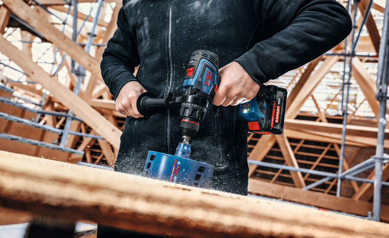 Person, die eine Akku-Schlagbohrmaschine bedient, um ein großes Loch durch Holz zu bohren