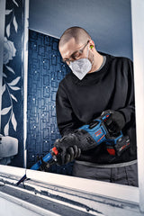 Eine Person mit Schutzausrüstung schneidet mit einer Bosch Expert Akku-Säbelsäge einen Fensterrahmen durch