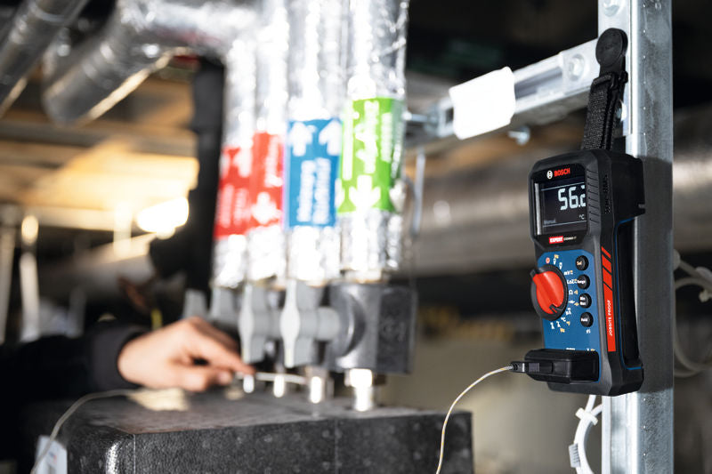 Eine Person inspiziert Rohre, während ein digitales Multimeter in der Nähe die Temperatur misst