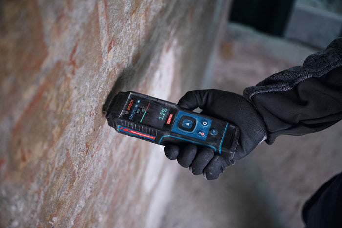 Eine Person mit Schutzausrüstung misst die Wandfeuchtigkeit mit einem digitalen Feuchtigkeitsmessgerät