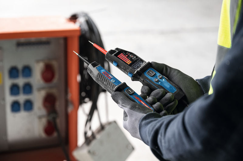Eine Person mit Sicherheitsausrüstung verwendet einen Spannungsprüfer in der Nähe einer Schalttafel