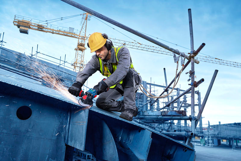 Eine Person mit Schutzausrüstung schleift Metallträger mit einem Akku-Winkelschleifer