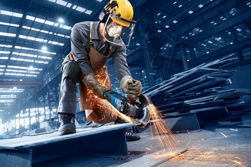 Eine Person mit Schutzausrüstung schneidet mit einem Winkelschleifer Metall und erzeugt dabei Funken