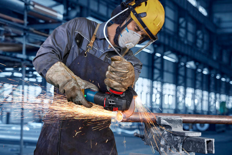 Eine Person mit Sicherheitsausrüstung schleift ein Metallrohr und erzeugt dabei helle Funken