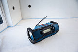 Auf dem Boden eines teilweise fertiggestellten Raumes steht ein robustes blaues Radio.