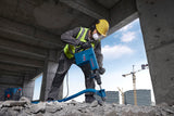 Eine Person in Schutzausrüstung sprengt Beton mit einem Abbruchhammer.