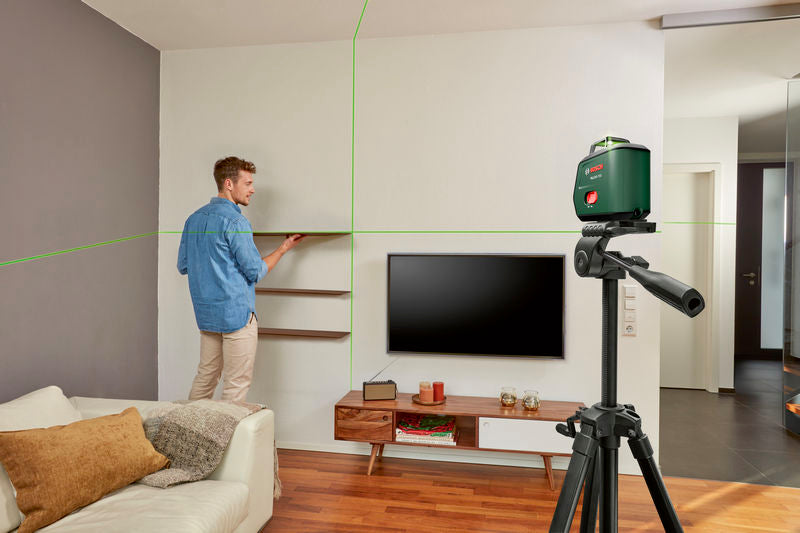 Eine Person montiert mithilfe eines Laser-Nivelliergeräts ein Regal in einem Wohnzimmer.
