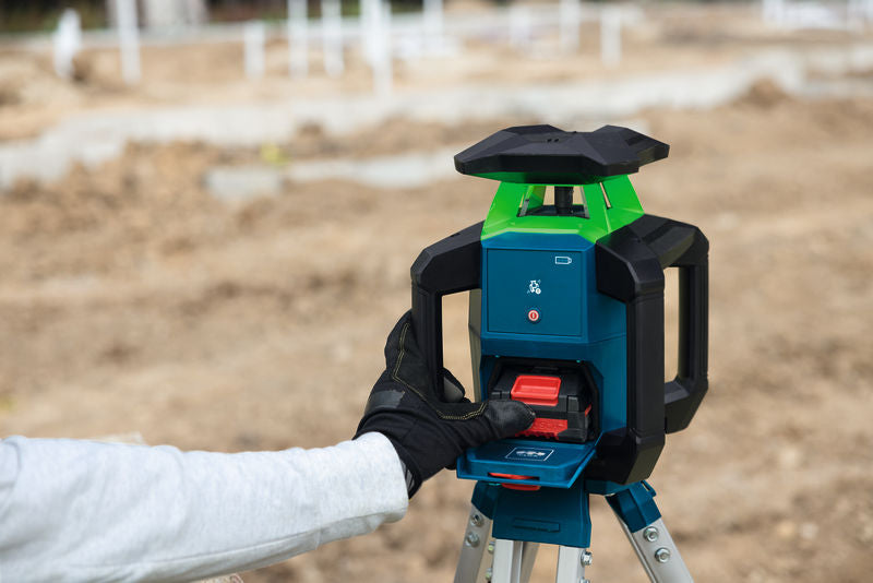 Eine Person in Schutzausrüstung justiert ein Laser-Nivelliergerät auf einer Baustelle.