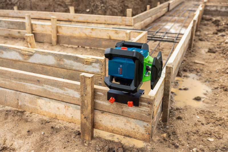 Auf einer schlammigen Baustelle ist ein Laser-Nivelliergerät auf einer Holzschalung aufgebaut.