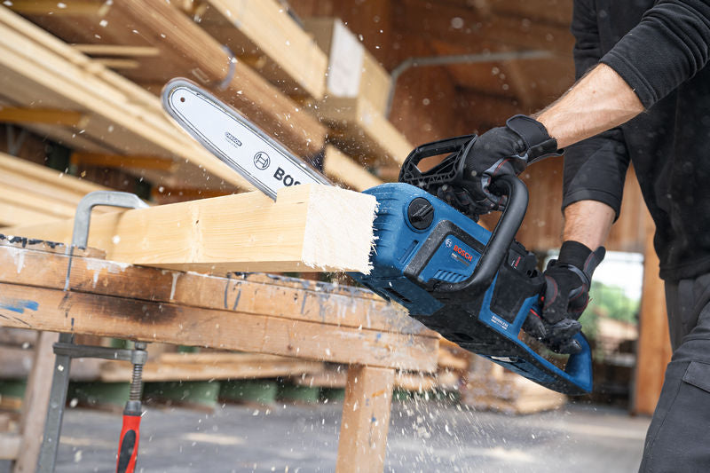 Eine Person, die Schutzausrüstung trägt, schneidet einen Holzbalken mit einer Akku-Kettensäge.