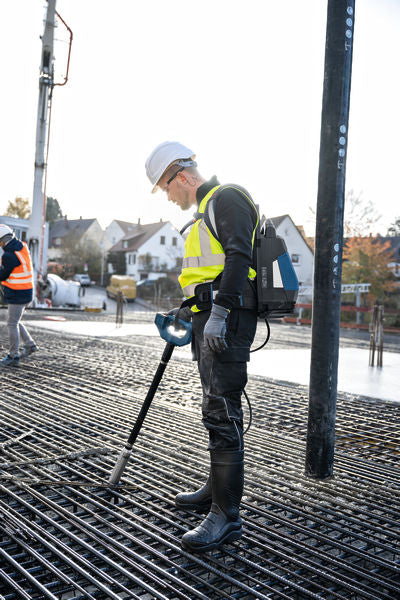 Eine Person, die Schutzausrüstung trägt, benutzt einen Betonrüttler auf einem Bewehrungsgitter.