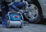 Eine Person in Schutzausrüstung benutzt einen Luftkompressor, um ein Autorad zu reinigen.